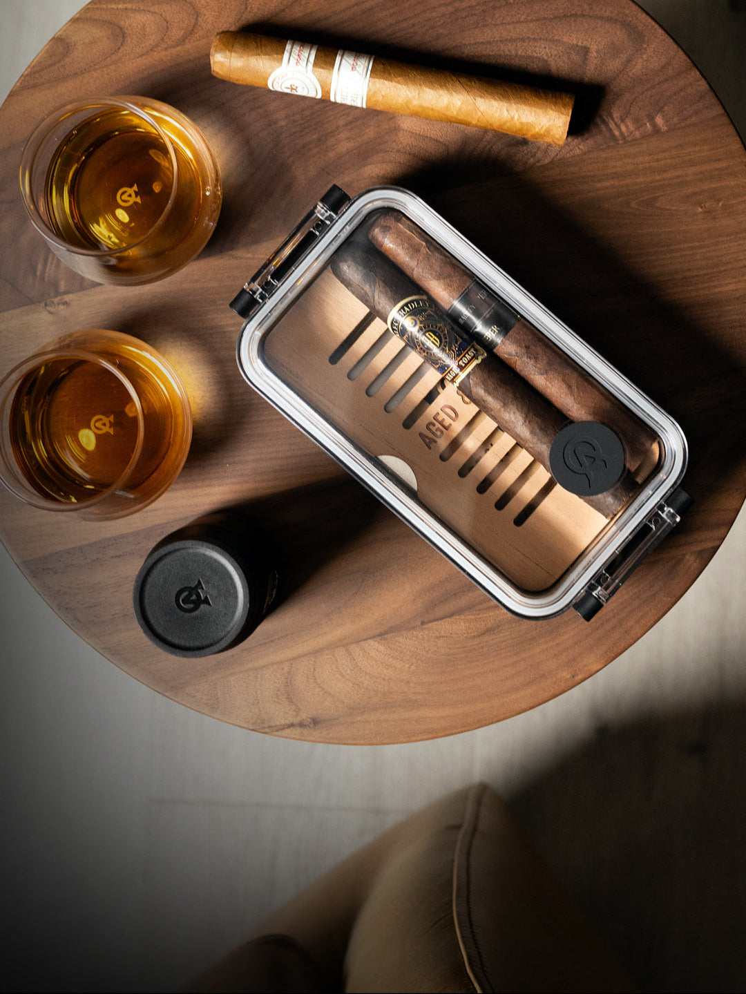 Cigar, glass of whiskey, and humidor on a wooden coaster.